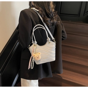 Silver wavy texture bucket bag with plush bear charm worn cross-body on black blazer