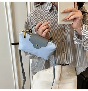 Detail of blue and grey trapezoid tote bag with gold zipper and leather flap