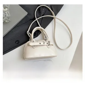 Detailed view of mini cream shell bag with adjustable strap beside a smartphone