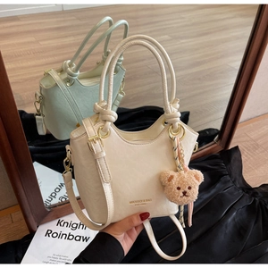 Détail du sac seau en PU crème avec logo doré, poignée nouée et breloque ours en peluche