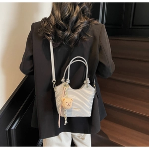 Rear view of a light gray wave pattern bucket bag with a plush bear and silk scarf decor