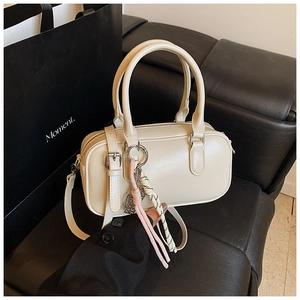 Détail d'un sac bowling crème avec pendentif tissé posé sur une surface en cuir noir