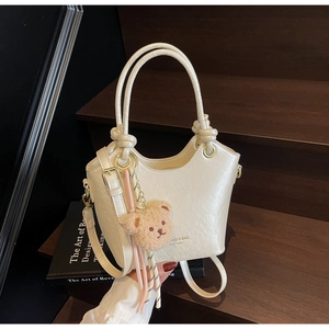 Détail d'un sac seau en PU blanc crème avec charm ourson brun sur des marches en bois
