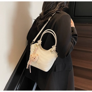 Detail of cream wavy texture bucket bag with knot handle and plush bear charm