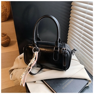 Détail d'un sac Boston en cuir PU noir brillant avec pendentif tissé dans un décor chic