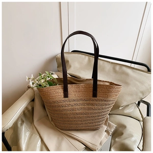 Detail of handwoven straw tote bag with brown leather straps on a beige chair