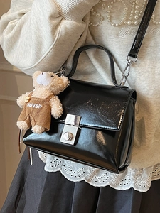 Minimalist black patent leather crossbody bag with top handle and a plush teddy bear charm