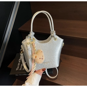 Détail d'un sac seau argenté avec texture métallisée et pendentif ours en peluche