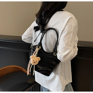 Detail of black wavy textured bucket bag with teddy bear charm and gold logo