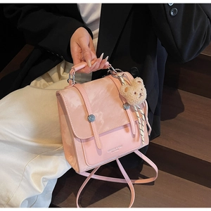 Pink faux leather shoulder bag with decorative bear pendant shown by model on stairs