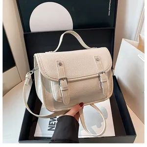 Detail of off-white lychee grain leather messenger bag with decorative buckles and top handle