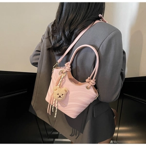 Pink bucket bag with wave texture and bear charm worn over the shoulder by a model