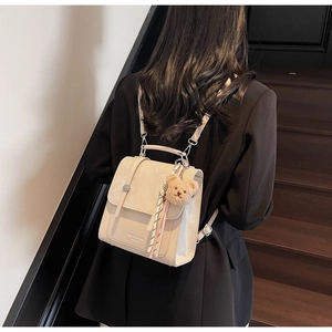 Detail view of a cream mini backpack with bear charm and ribbon on model's back