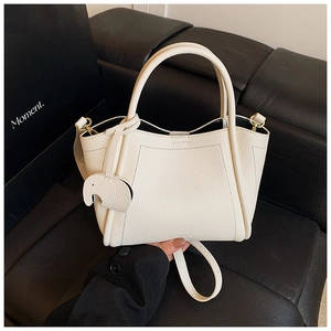 Detailed view of white litchi pattern bucket bag with cute elephant charm on leather sofa