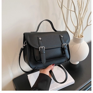 Detail of black pebbled leather messenger bag with metal buckle straps and top handle