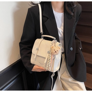 Detail of cream white leather crossbody bag with metal clasp and brown plush bear charm