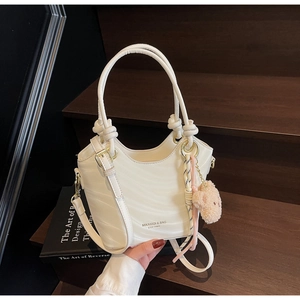 Detail of off-white wave textured bucket bag with knotted handle and brown bear charm