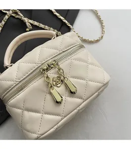 Détail du sac boîte beige matelassé avec fermeture éclair dorée et breloque fleur de camélia