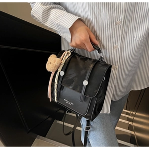 Detail view of black leather flap handbag with vertical buckle straps and plush bear charm