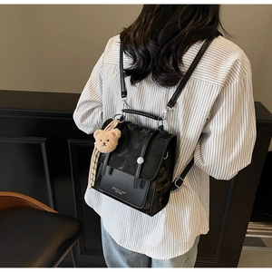 Detail view of the black PU leather backpack with brand logo and cute plush bear charm