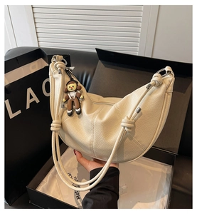 Close-up of beige crescent bag with lychee grain leather and cute doll pendant