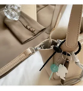 Close-up of beige lychee texture leather bucket bag with creative charms and silver hardware