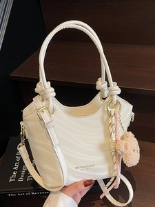 Elegant wave textured cream bucket bag with knot handle and plush bear charm on a staircase