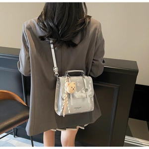 Detail view of a silver metallic crossbody bag with a plush bear charm on a model
