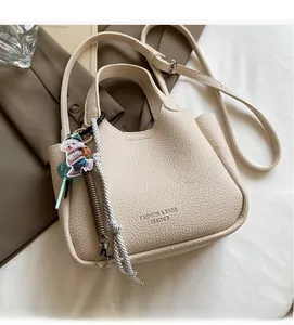 Detail of lychee textured cream leather handbag with bear charm and woven strap