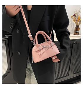 Close-up of a pink semi-circular handbag with silver buckles held by a model in a black blazer