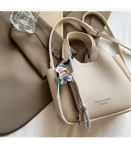 Detail of beige lychee pattern leather bucket bag with cute dog charm and decorative charms