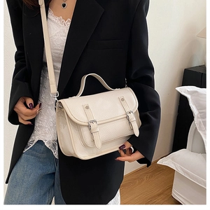 Detailed close-up of cream messenger bag showing lychee leather texture and buckle straps