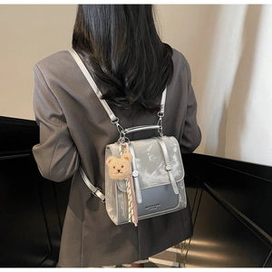 Detail of silver metallic backpack with plush bear charm and tassel on a model