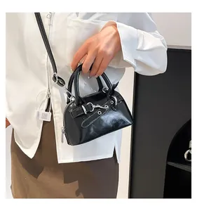 Detail of a black patent leather mini shell bag with silver rivets and zippers in moto style