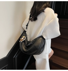 Detail of black soft leather hobo bag featuring knotted shoulder strap and monkey charm