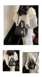 Detail of black lychee grain leather bucket bag with cute bear charm and woven strap