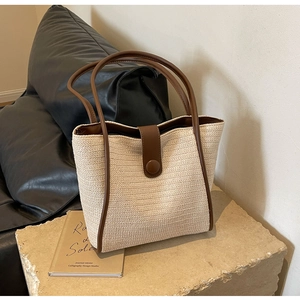 Detail of woven straw tote bag featuring brown leather trim and circular buckle closure