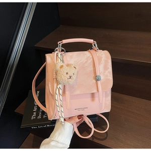 Detailed view of pink leather backpack with a plush bear charm on a vintage wooden step