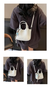 Detail view of off-white lychee grain bucket bag with charm and shoulder strap