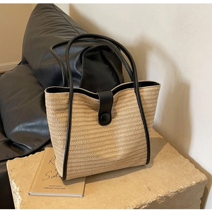 Detail of woven straw tote bag with black leather trim on a textured stone surface