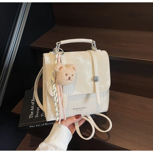 Detail view of cream white PU leather backpack with cute bear pendant on wooden stairs