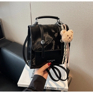 Detail view of black glossy mini backpack with brand logo and cute plush bear charm accessory