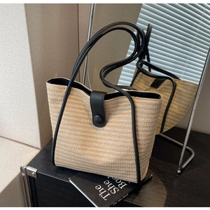 Detail of woven tote bag with black leather trim and magnetic buckle on dark wood table