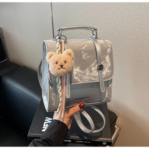 Detailed shot of shiny silver backpack with bear charm and square buckle closure