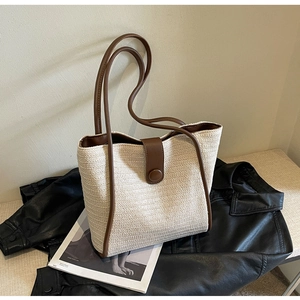 Detail of woven tote bag with brown leather trim and magnetic buckle on black background