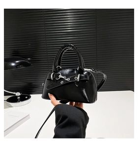 Close-up of black patent leather shell bag featuring silver metal eyelets and punk style strap