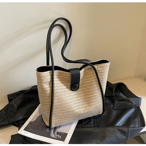 Close-up of woven straw tote bag with black leather trim and decorative buckle detail