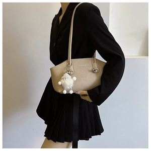 Detail view of beige shoulder bag with silver text and a white fluffy monster charm accessory