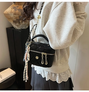 Détail du sac matelassé noir avec logo camélia doré et pompon tissé sur la bandoulière