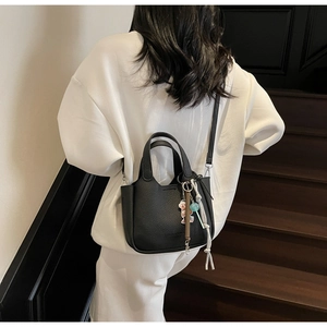 Detail of black lychee grain leather bucket bag with cute bear charm and tassel accessory
